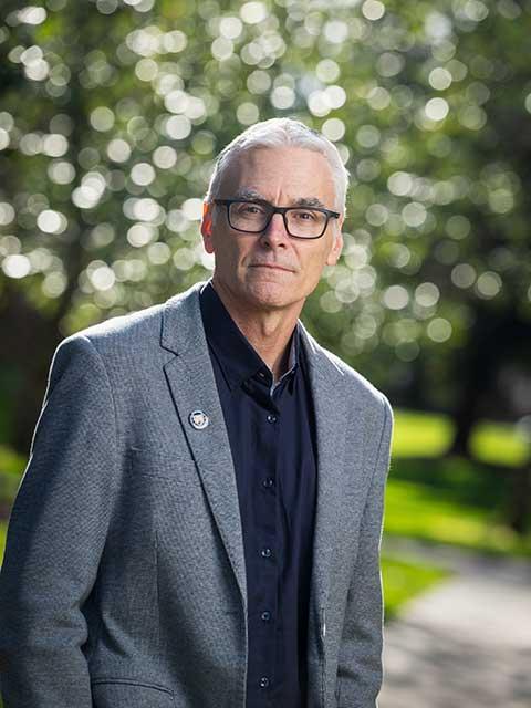 Todd Palmer, standing in a grey suit in front of trees